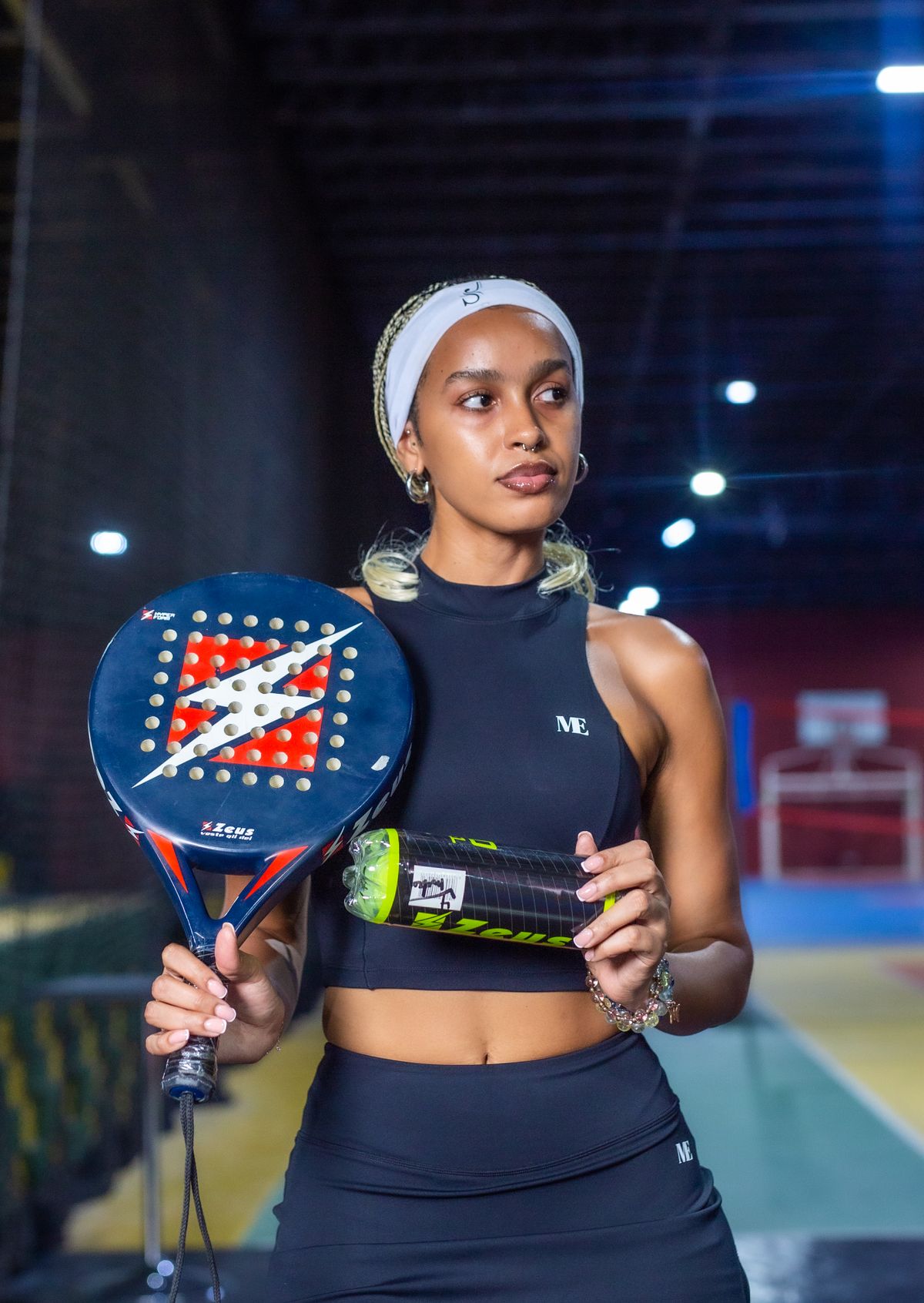 Speelster in padelkleding met racket en ballenkoker op een indoorbaan